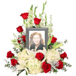 Memorial floral arrangement with red roses, white lilies, and a framed portrait