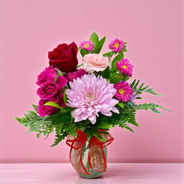 Bouquet of pink and red flowers in a glass vase with a red ribbon