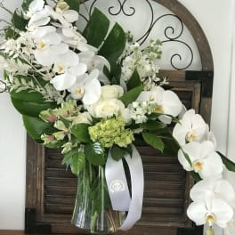 White orchid and rose arrangement in a glass vase with green accents