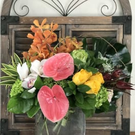 Mixed tropical bouquet in a glass vase with pink anthuriums and yellow roses
