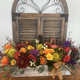 Colorful mixed flower arrangement in a wooden container with a plaid ribbon