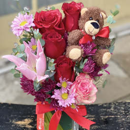 Bouquet of red roses and pink flowers with a teddy bear in a glass vase