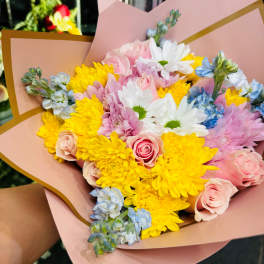 Bouquet of pink roses, yellow chrysanthemums, and white daisies in pink wrap