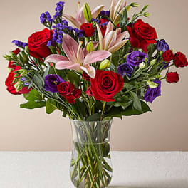 Bouquet of red roses, pink lilies, and purple flowers in a glass vase