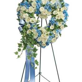 Heart-shaped floral wreath with white and blue flowers on a stand