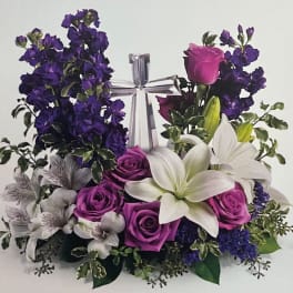 Purple and white floral arrangement with roses and lilies around a silver gift box