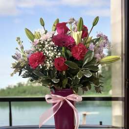 Pink and purple mixed bouquet in a magenta vase with a ribbon