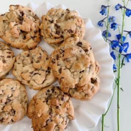 Plate of chunky chocolate chip cookies with blue flowers beside it on a white surface