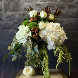 White rose and hydrangea arrangement with trailing greenery in a glass vase