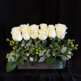 White roses arranged in a wooden box with green berries and foliage