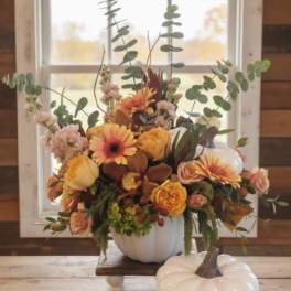 Autumn arrangement of orange and yellow flowers in a white pumpkin vase with matching pumpkin jar.