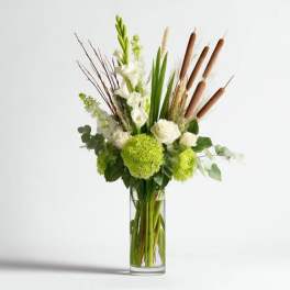 Tall green and white arrangement with hydrangeas, roses, and cattails in a clear glass cylinder vase