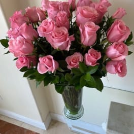 Tall arrangement of pink roses in a clear glass vase on a glass table