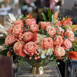Peach rose arrangement in a gold vase with white accents and autumn foliage