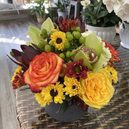 Mixed bouquet with roses, orchids, and yellow daisies in a dark vase