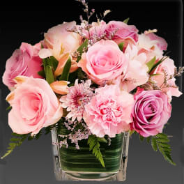Pink and lavender roses with carnations and mums in a square glass vase.