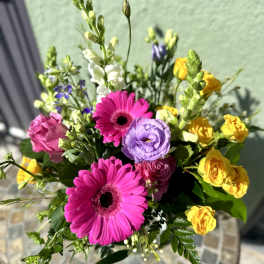 Bright bouquet with hot pink gerbera daisies, yellow spray roses, purple lisianthus, and white snapdragons