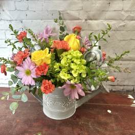 Mixed bouquet in a metal watering can with pink, yellow, and coral flowers