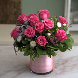 Low arrangement of hot pink roses with white accents in a pink-wrapped glass cylinder vase
