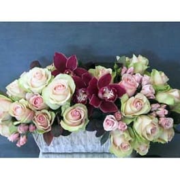 Arrangement of pale roses and burgundy orchids in a rectangular container