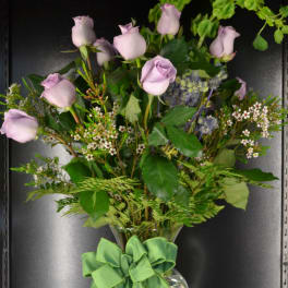 Lavender roses in a clear glass vase with a green ribbon