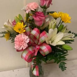 Bouquet of pink roses, lilies, and yellow daisies in a glass vase with a plaid ribbon