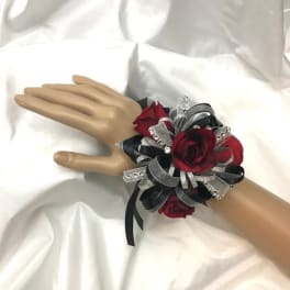 Red rose wrist corsage with black and silver ribbon on a mannequin hand