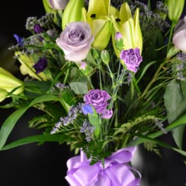 Bouquet of lavender roses and yellow lilies with a purple ribbon