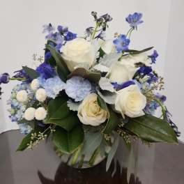 White roses and blue flowers arranged in a glass vase