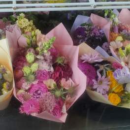 Assorted pastel-wrapped mixed flower bouquets arranged together in a cooler case