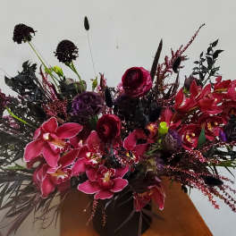 Large arrangement of pink orchids and dark red flowers in a vase