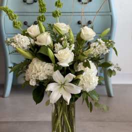 White floral arrangement in a clear glass vase with lilies and roses