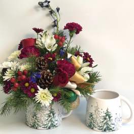 Holiday floral arrangement in a winter-themed mug beside a matching mug