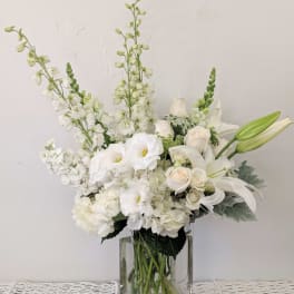 White floral arrangement in a clear glass vase with lilies and roses