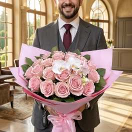 Man in a suit holding a large pink bouquet with roses and white orchids