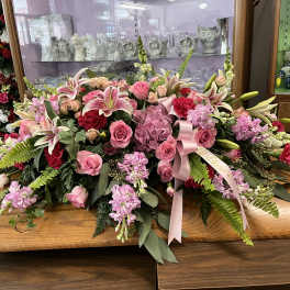Large pink floral spray with lilies, roses, and ribbon on a wooden table