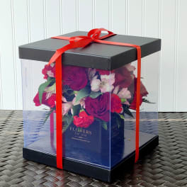Boxed bouquet of red and pink flowers tied with a red ribbon