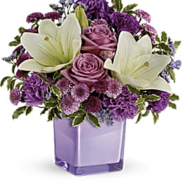 Purple and white floral arrangement in a lavender glass vase