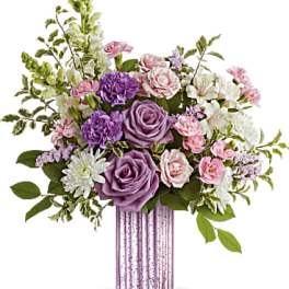 Tall bouquet of purple roses, pink spray roses, and white flowers in a ribbed lavender glass vase