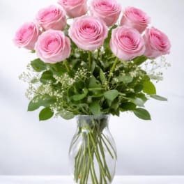 Arrangement of pink roses with white filler flowers in a clear glass vase