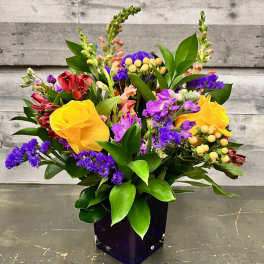 Mixed bouquet with yellow roses and purple flowers in a dark vase
