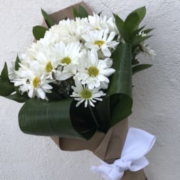 Bouquet of white daisies wrapped in brown paper with a white ribbon