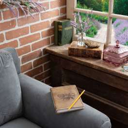 A small vase of purple flowers sits on a wooden table by a window.