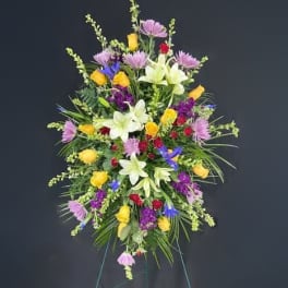 Tall standing spray with yellow roses, white lilies, and mixed purple flowers on an easel