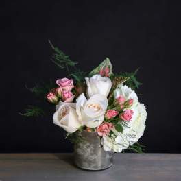 Short arrangement of white roses, pink spray roses, and white hydrangea in a silver vase