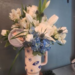 Tall arrangement of white and blue flowers in an evil-eye patterned ceramic tumbler