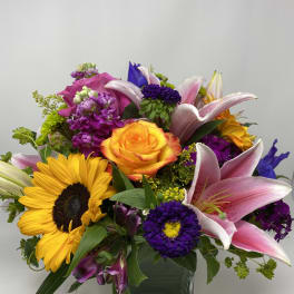 Mixed bouquet with sunflowers, pink lilies, and an orange rose in a glass vase