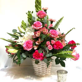 Pink roses and lilies arranged in a woven basket with greenery