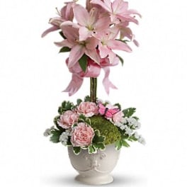 Tall pink lily topiary with pink carnations and white filler flowers in a white ceramic urn.