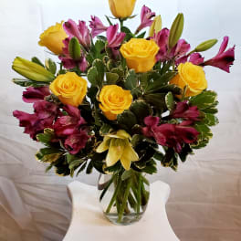 Yellow roses and magenta lilies arranged in a glass vase